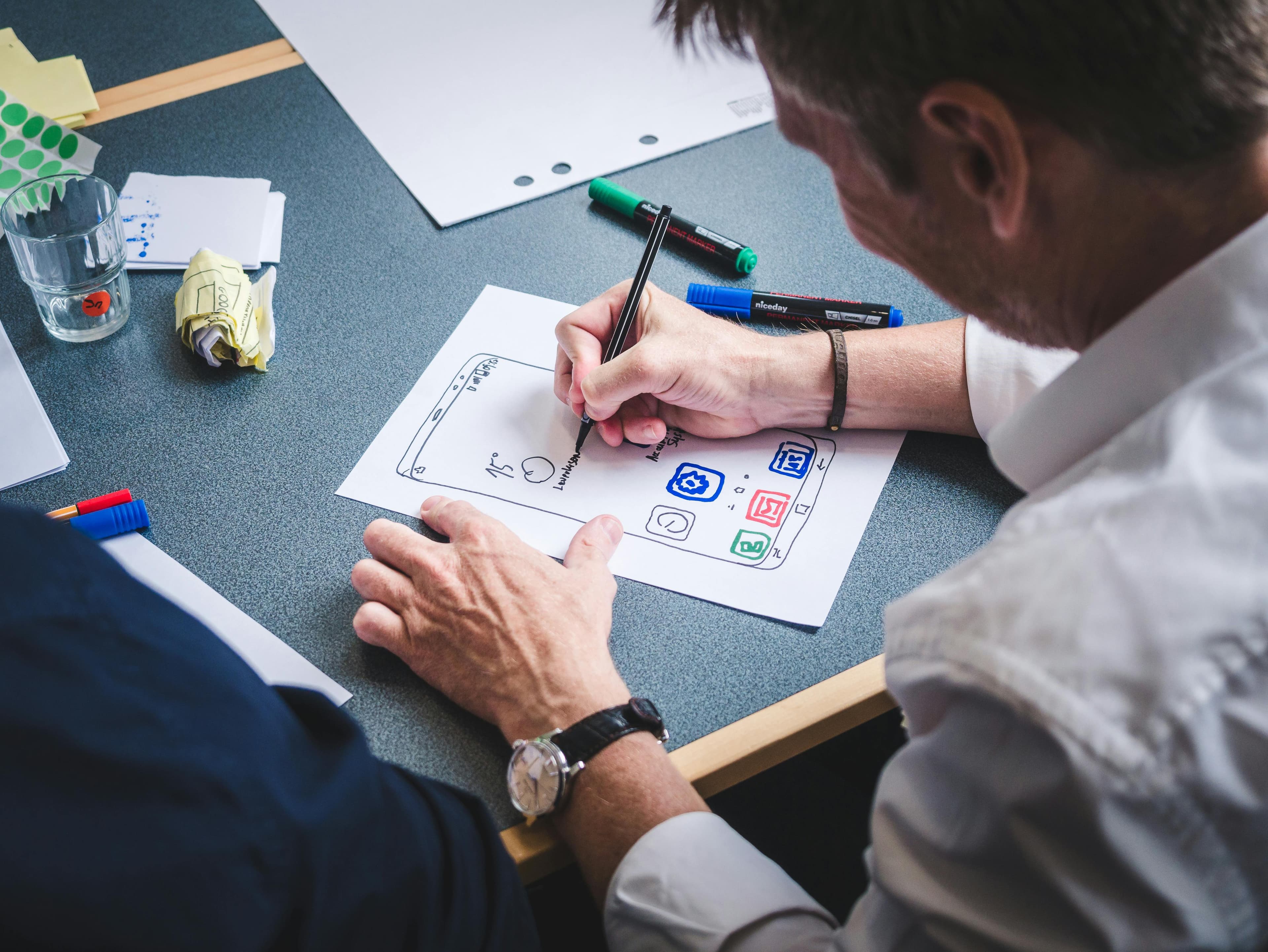 A designer sketching a mobile app wireframe on paper at a desk